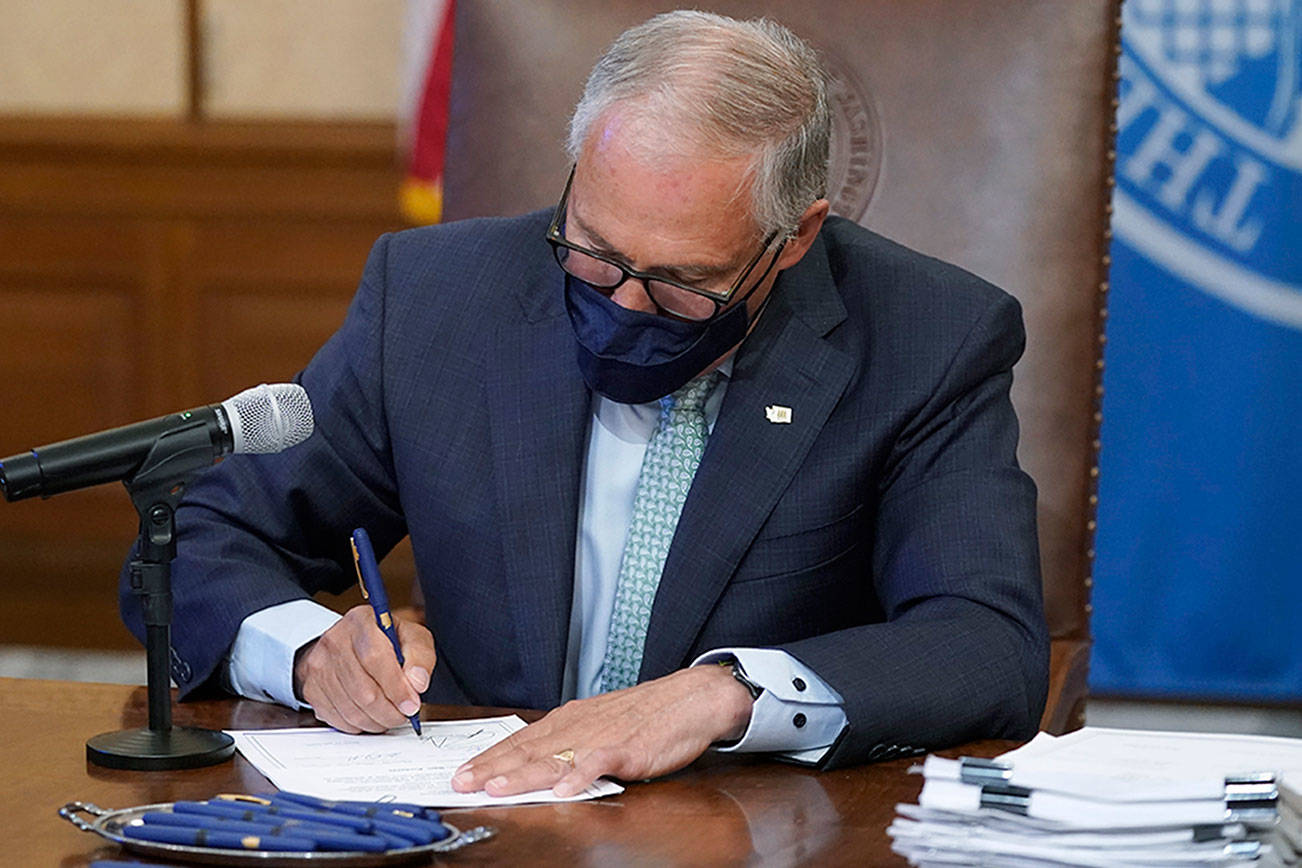 Washington Gov. Jay Inslee signs a bill into law, Wednesday, May 12, 2021, at the Capitol in Olympia, Wash., that prohibits openly carrying guns and other weapons at the state Capitol and protests statewide. (AP Photo/Ted S. Warren)