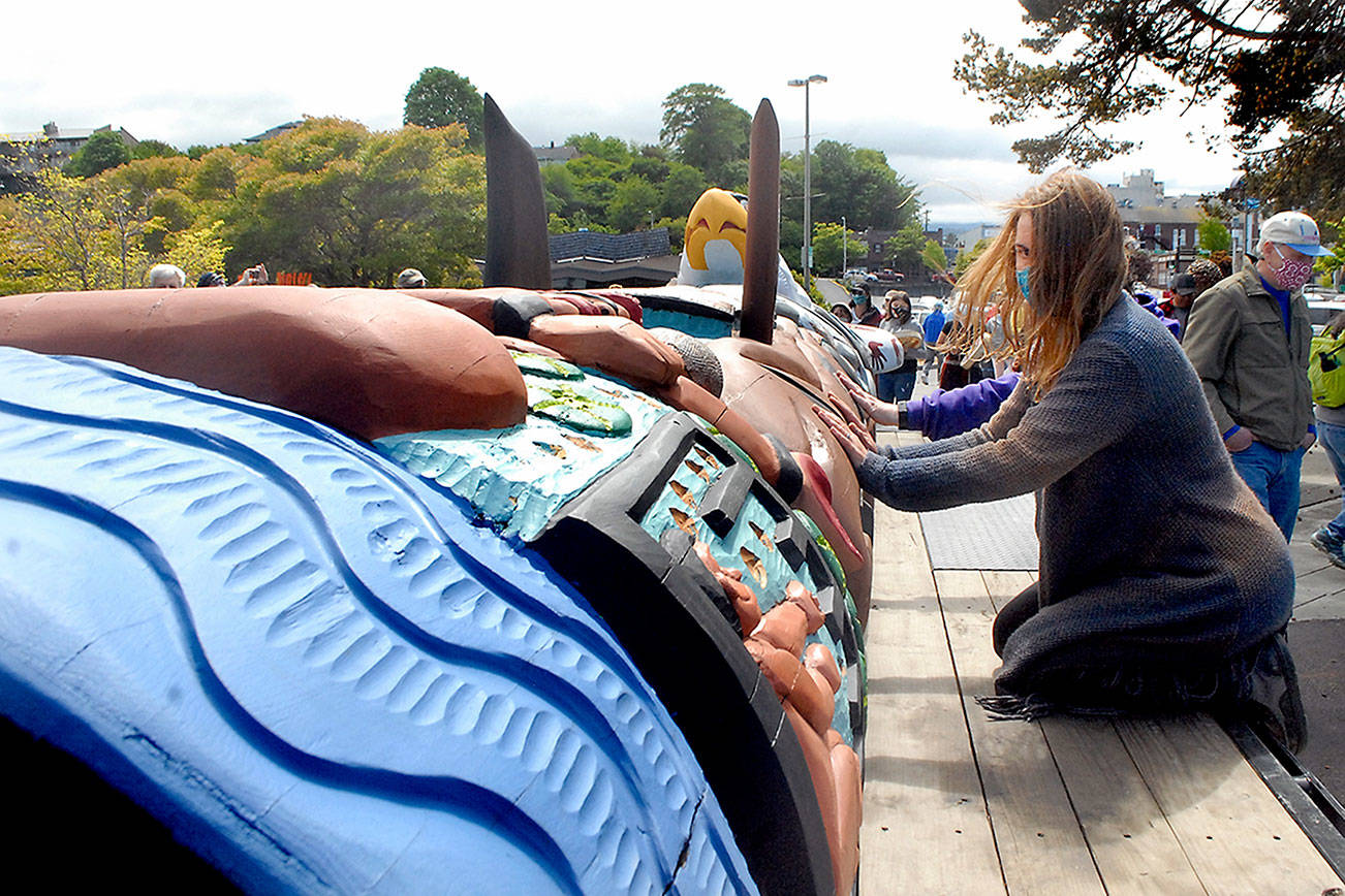 Julia Buggy of Sequim knees on a flatbed trailer as she lays her hands on a traveling totem created by carvers from the Lummi Nation during a stop on Tuesday at Port Angeles City Pier. (Keith Thorpe/Peninsula Daily News)