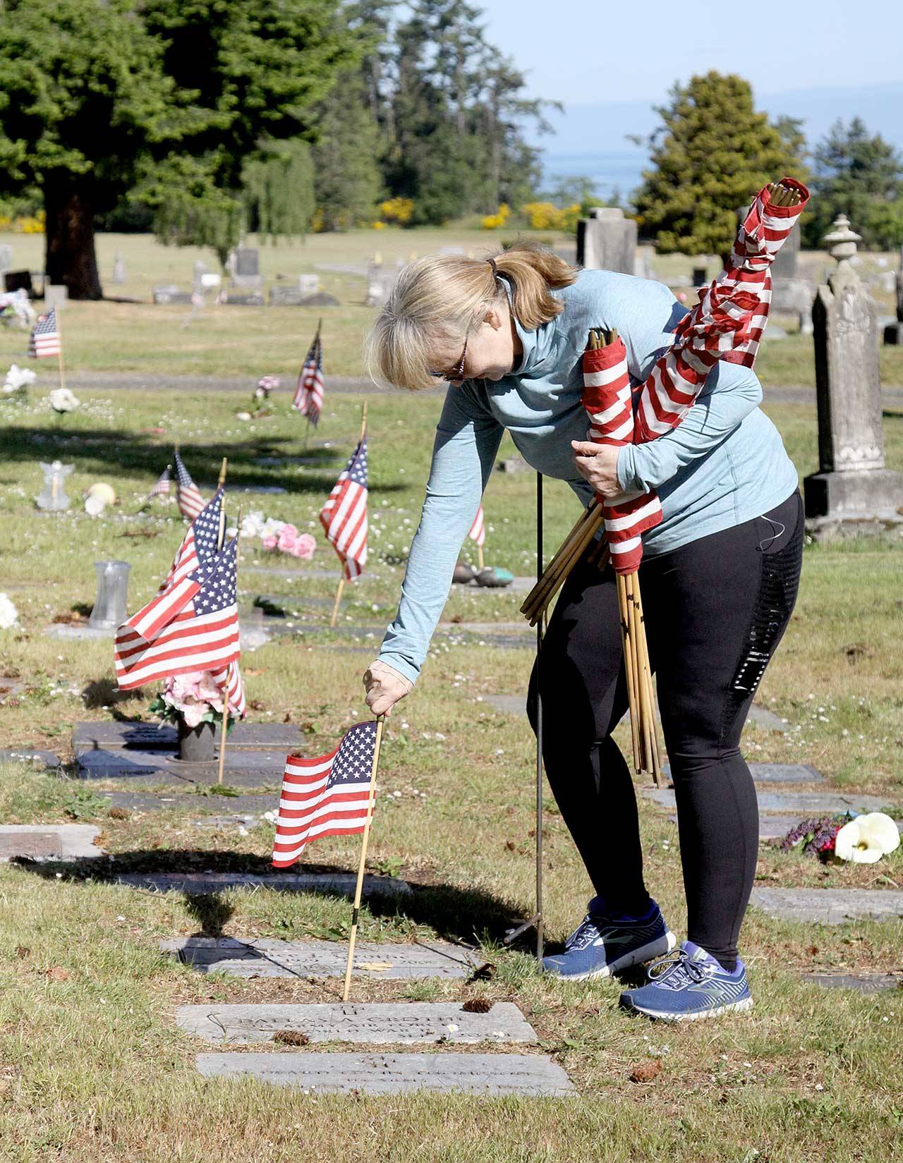 American Legion member Patricia Radford uses a sharp tool to poke a hole in the ground and then places an American flag near the grave of a service member. In preparation for Memorial Day, volunteers went to Ocean View Cemetery to place small flags on all the graves of former service members they could locate. They placed hundreds of flags Saturday morning to honor and remember those who gave their service to the country. (Dave Logan /for Peninsula Daily News)