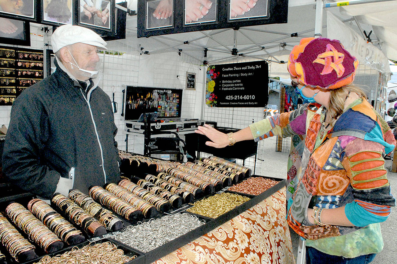 Keith Thorpe/Peninsula Daily News 

Saffrel Cochon of Monroe, right, tries on a bracelet as vendor Larry Rankin of Leavenworth-based Art to Suit You looks on at the Juan de Fuca Festival street fair outside the Vern Burton Community Center in Port Angeles. Admission to the fair, which runs through 6 p.m. today, is free. In-person concerts inside the community center continue today with limited tickets. More than 20 performances from multi-genre bands, singer-songwriters, dance ensembles and solo artists across North America are available for streaming on demand until June 30. More details are at JFFA.org/festival.