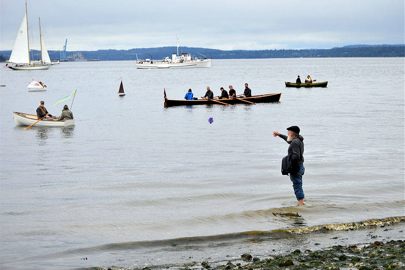 Len Feldman sends flowers to Port Townsend Bay in honor of Brion Toss, the famed rigger, teacher and author who died in June 2020. The smallest boat on the water, a one-fifth scale model of a 1933 Sam Crocker-designed catboat named Katy, was launched during the procession Wednesday morning; it bears Toss’ ashes. (Diane Urbani de la Paz/Peninsula Daily News)