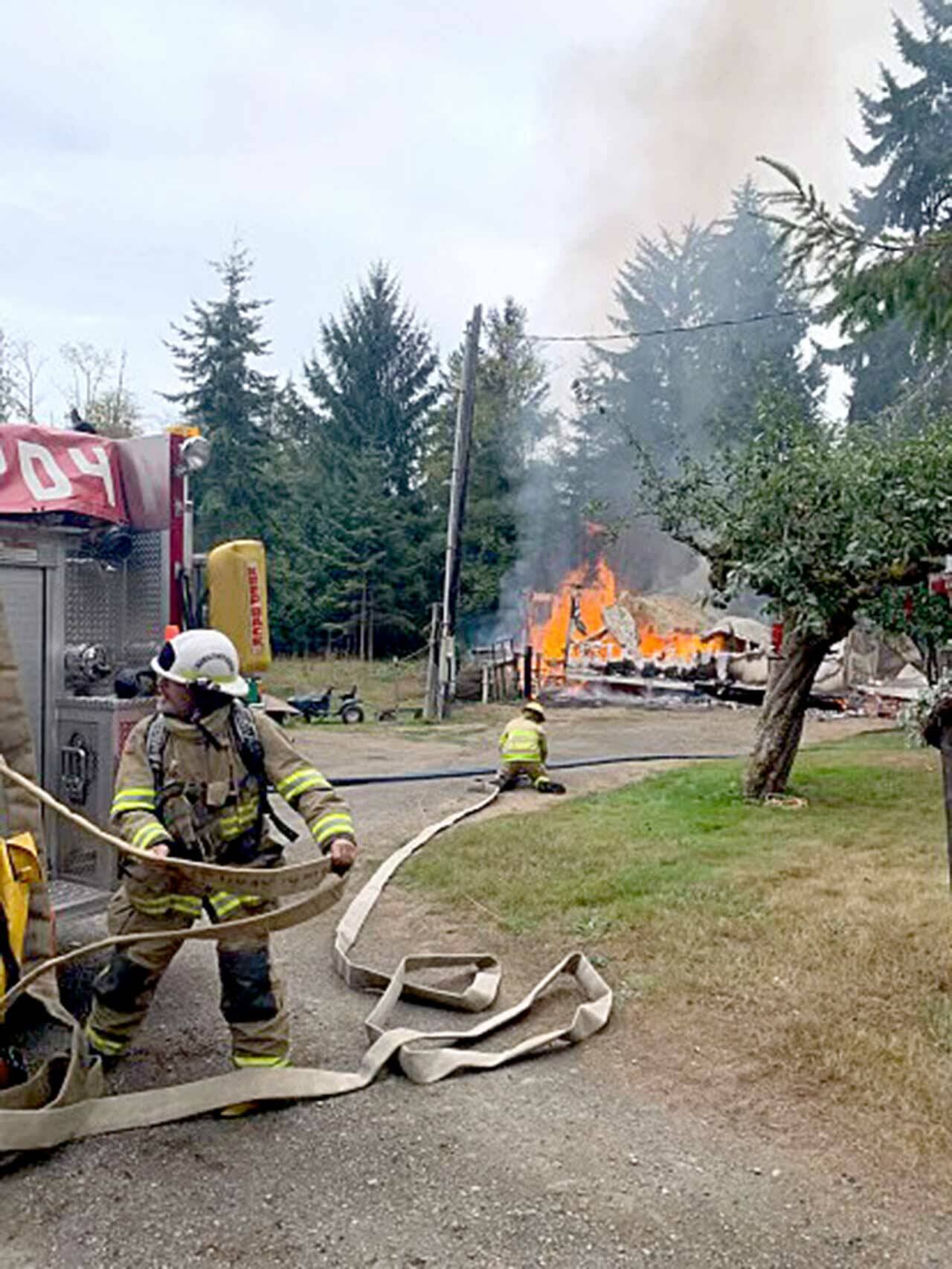 Clallam County Fire District 4 Assistant Fire Chief Alex Baker rolls out a hose Sunday to fight a fire west of Joyce while firefighter Brett Frantz sets up and gets ready for water. (Clallam County Fire District 4)