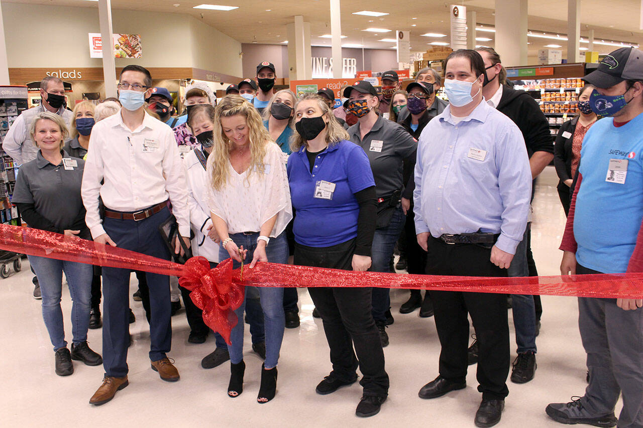 Rachel Hill, the e-commerce lead for the Port Townsend Safeway, cuts the ribbon during the store’s “Grand Reopening” on Wednesday while surrounded by current and retired employees of the store. (Zach Jablonski/Peninsula Daily News)