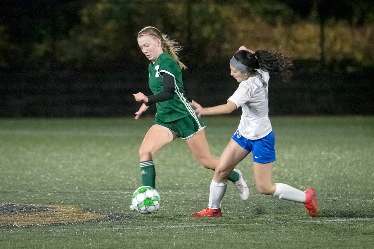 Jesse Major/for Peninsula Daily News Port Angeles sophomore Izzy Felton dribbles by Olympic’s Autumn Clark during the Roughriders 4-0 Bi-District win over the Trojans at Peninsula College’s Wally Sigmar Field on Thursday