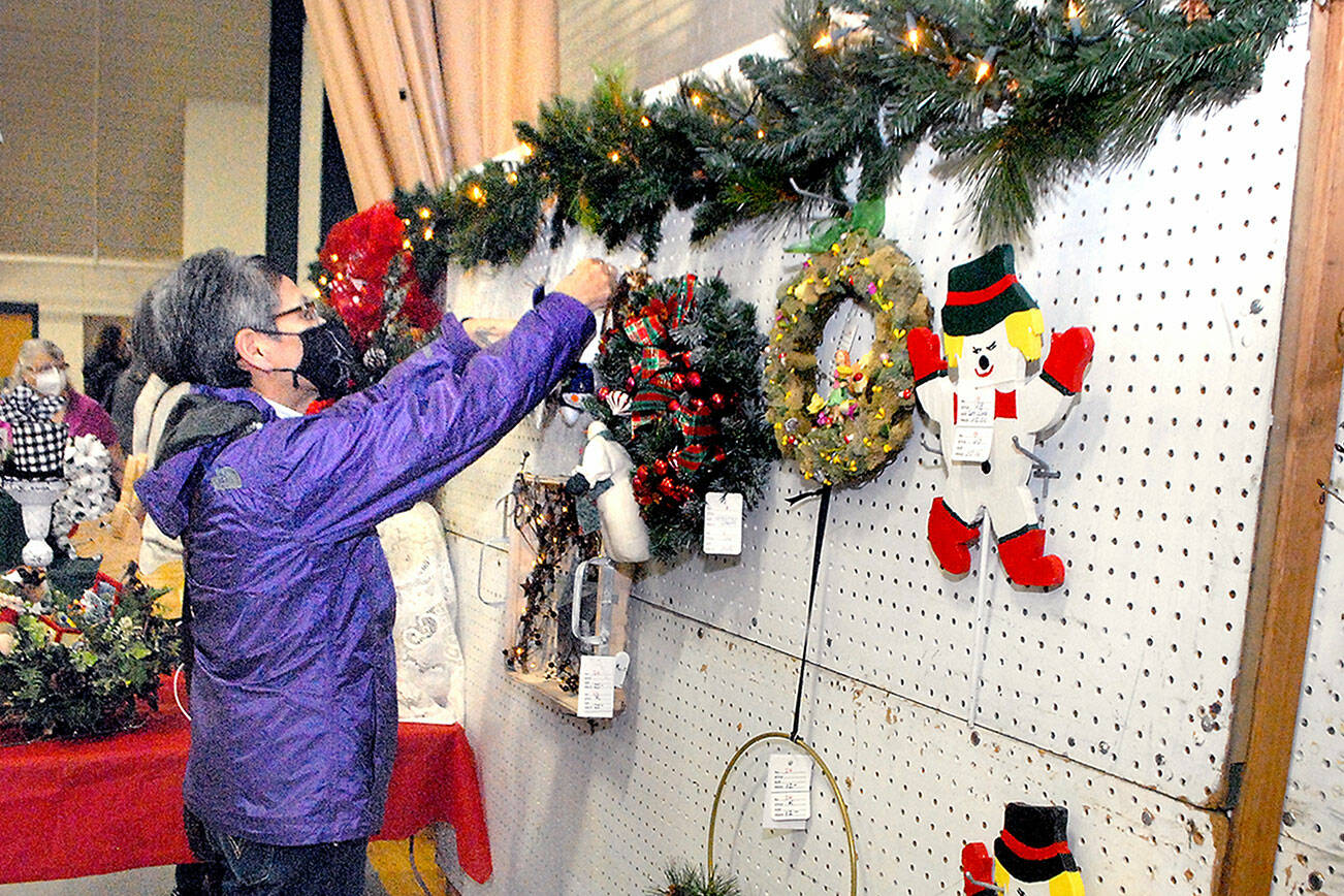 Marla Tolliver of Neah Bay examines wreaths and hanging holiday decorations on Saturday at the annual Christmas Cottage craft fair at Vern Burton Community Center in Port Angeles. The free event, which continues Sunday from 10 a.m. to 4 p.m., features a wide variety of holiday crafts created by a collection of local artists and artisans. (Keith Thorpe/Peninsula Daily News)