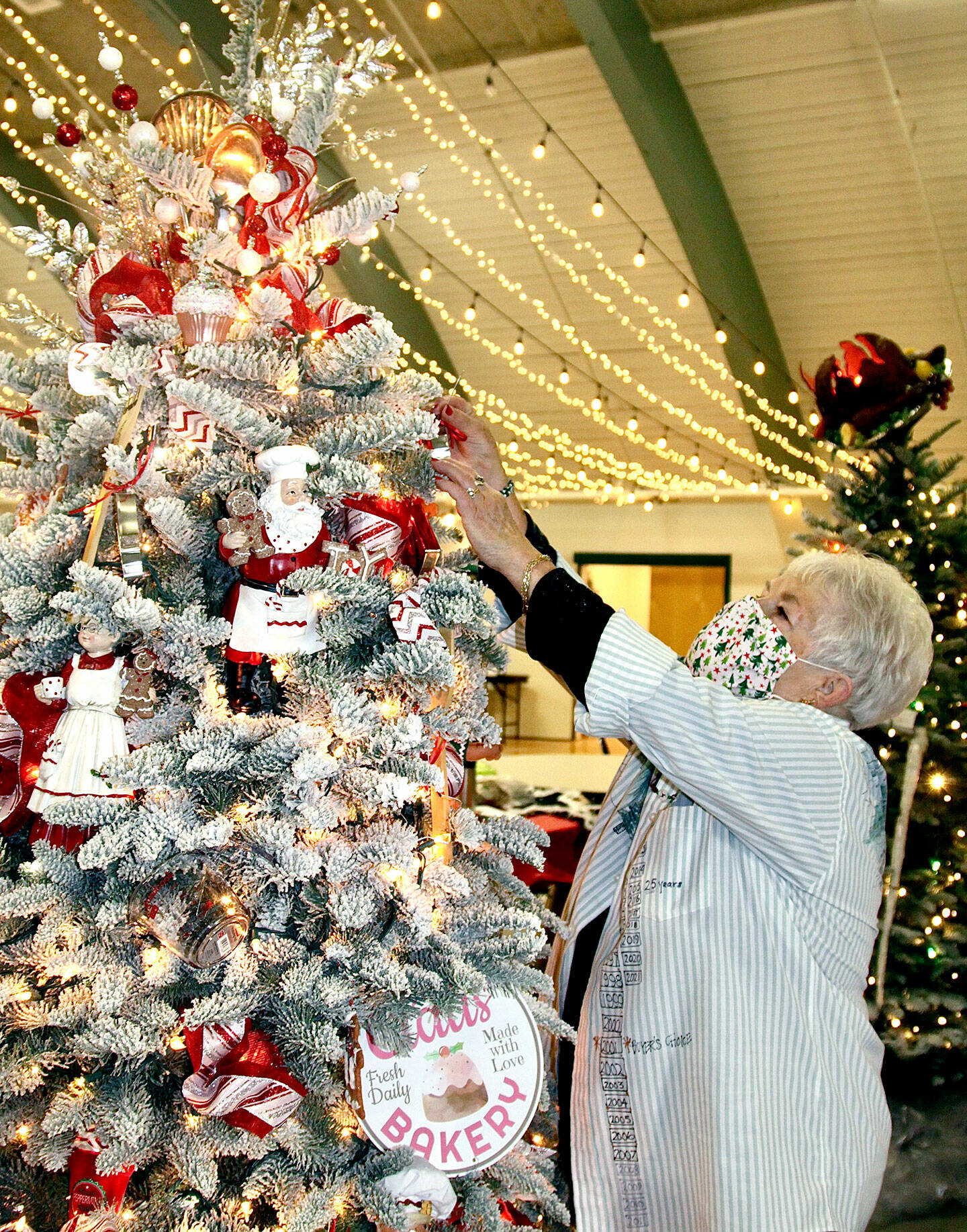 Sherry Phillips, the head of the designers group for the 31st edition of the Festival of Trees, puts another delight on her tree, called “Baking With Mrs. Santa,” earlier this week. Decorated trees will either be auctioned at the gala or by silent auction, all part of the Olympic Medical Center Foundation fundraiser inside the Vern Burton Center in Port Angeles. (Dave Logan/for Peninsula Daily News)