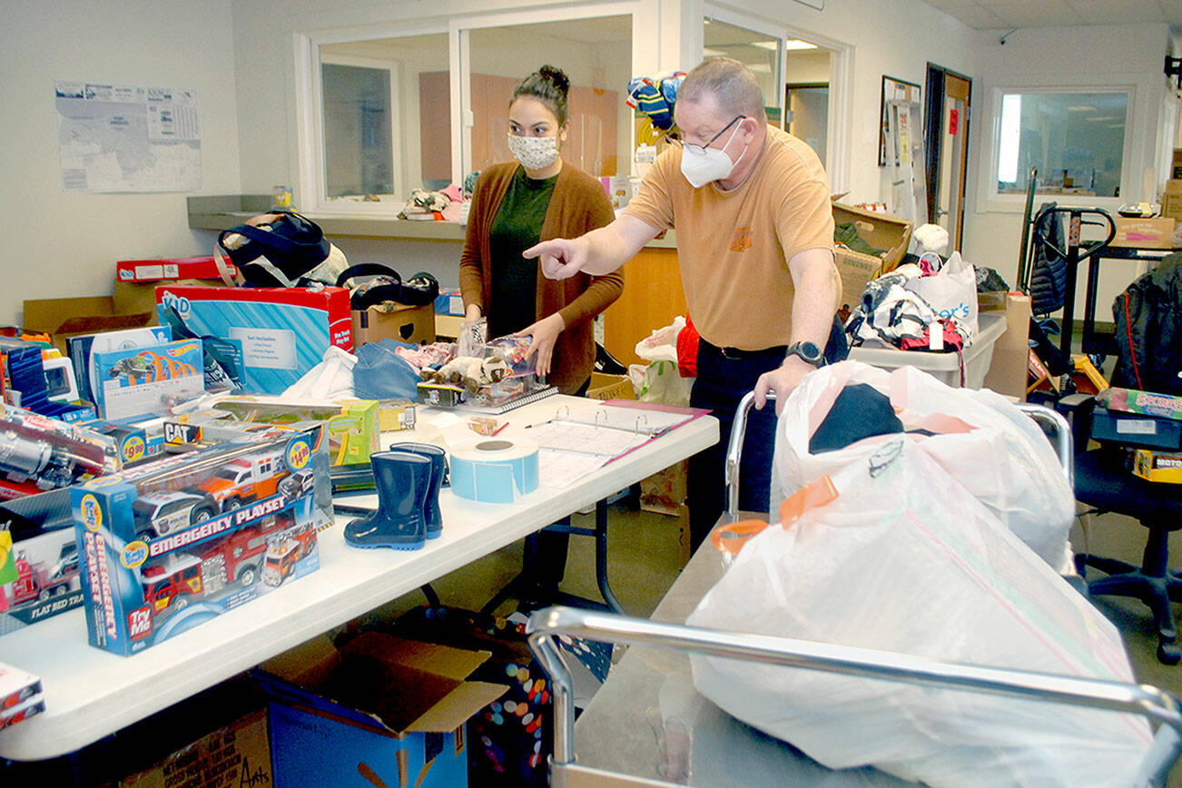 Deseree Garza, a representative of First Federal, left, and Salvation Army Major Ron Wehnau assemble bundles of Christmas presents for the organization’s Angel Tree program on Tuesday at the Salvation Army Community Center in Port Angeles. Major Barbara Wehnau said 201 families representing more than 500 children would be given packages of presents for the 2021 holiday season. (Keith Thorpe/Peninsula Daily News)