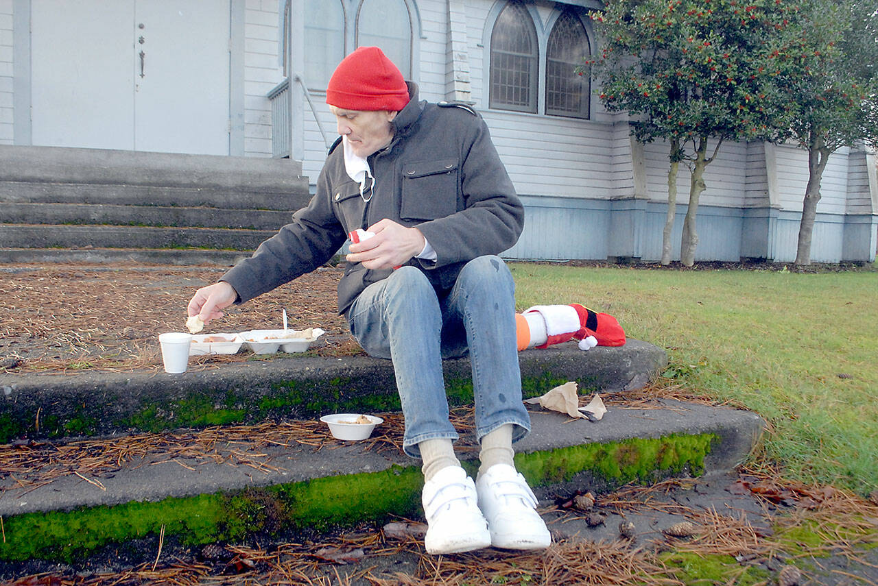 Michael Freestone of Port Angeles sits on the steps in front of the Salvation Army Church in Port Angeles as he enjoys a carry-out Christmas Eve lunch. The organization served dozens of lunches with an outdoor dining twist in its annual holiday tradition. (Keith Thorpe/Peninsula Daily News)