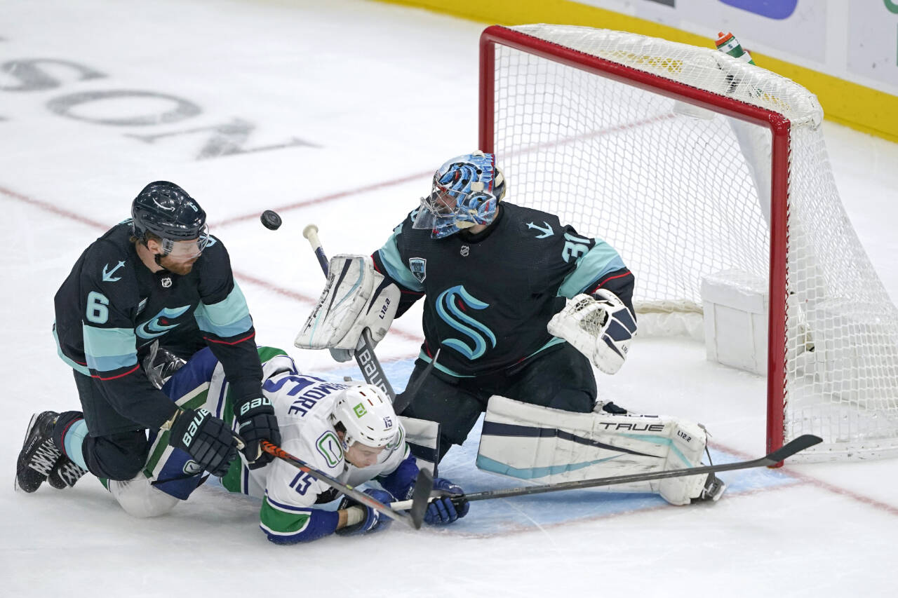 Seattle Kraken goaltender Philipp Grubauer, right, makes a stop as Kraken defenseman Adam Larsson (6) and Vancouver Canucks center Matthew Highmore (15) crash against him during the second period of an NHL hockey game Saturday, Jan. 1, 2022, in Seattle. (AP Photo/Ted S. Warren)