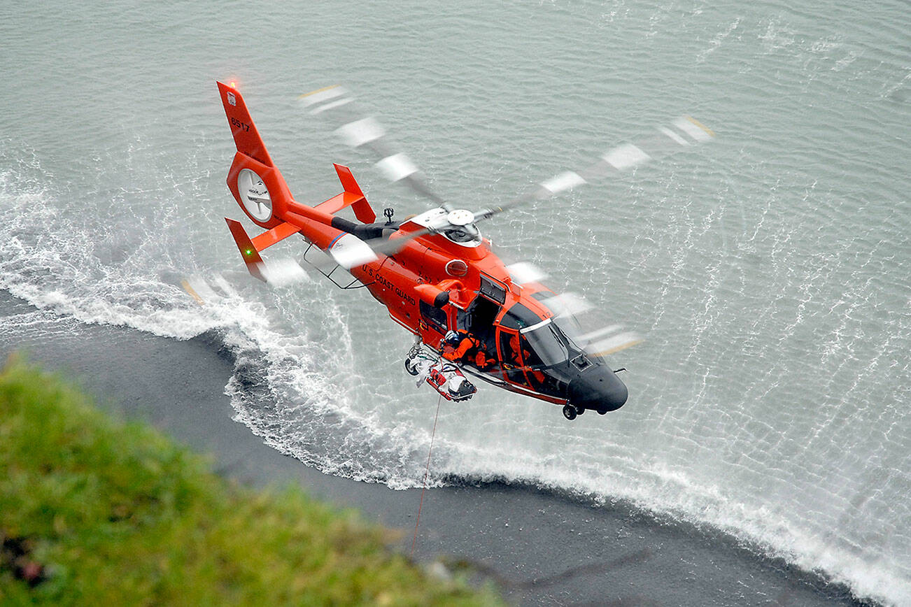 A U.S. Coast Guard helicopter hoists an injured person from the beach at the base of a bluff below 10th and Walker streets on the west side of Port Angeles on Wednesday. (Keith Thorpe/Peninsula Daily News)