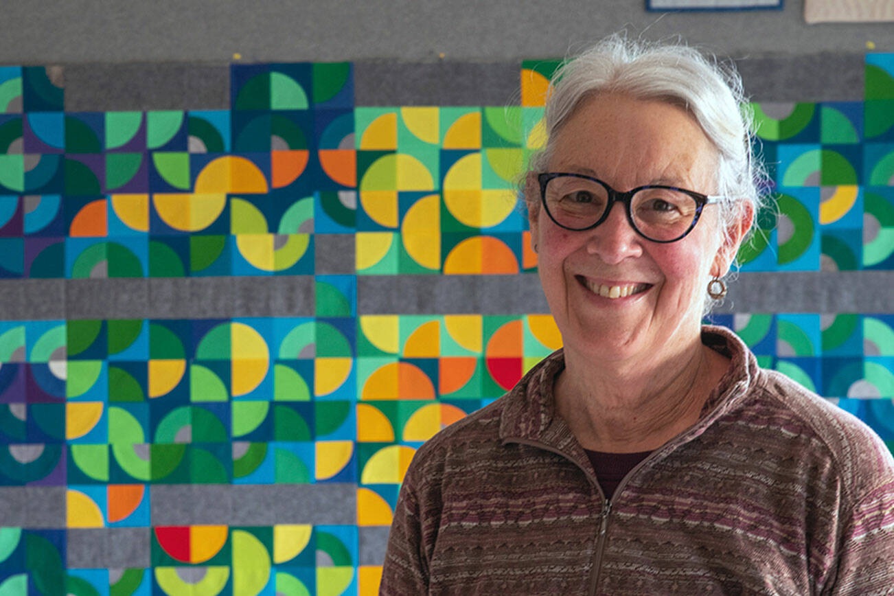 Fiber Artist Marla Varner stands in front of her temperature quilt. Each square is color coded to the high and low temperatures of each day of 2021 in her neighborhood in Sequim, with the smallest quarter circles signifying precipitation. (Emily Matthiessen/Olympic Peninsula News Group)