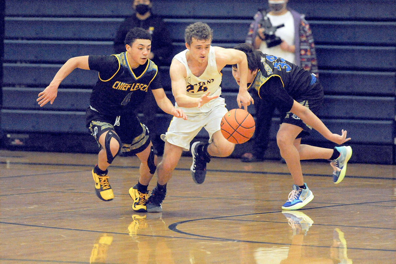 Forks’ Logan Olson, center, drives between Chief Leschi defenders Mickey Lara, left, and Emanual Mowat during the Spartans’ 68-54 win over the Warriors on Wednesday. (Lonnie Archibald/for Peninsula Daily News)