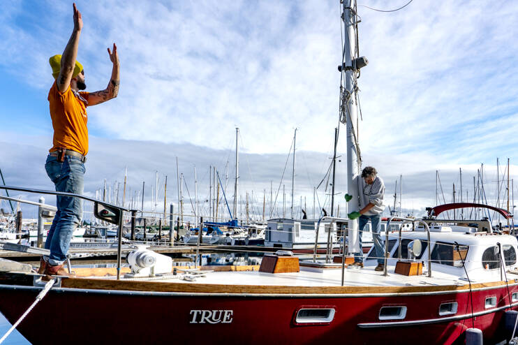 On Monday’s sun-drenched skies, Ben Doerr of Bainbridge Island directs a crane operator while Port Townsend rigger Sean Ranking, from Northwest Sails and Canvas, guides the mast into Doerr’s 44-foot Pierson Countess motor sailer. Doerr did a refit on his charter boat, True, including updates and wiring. (Steve Mullensky/for Peninsula Daily News)