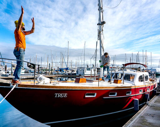 On Monday’s sun-drenched skies, Ben Doerr of Bainbridge Island directs a crane operator while Port Townsend rigger Sean Ranking, from Northwest Sails and Canvas, guides the mast into Doerr’s 44-foot Pierson Countess motor sailer. Doerr did a refit on his charter boat, True, including updates and wiring. (Steve Mullensky/for Peninsula Daily News)