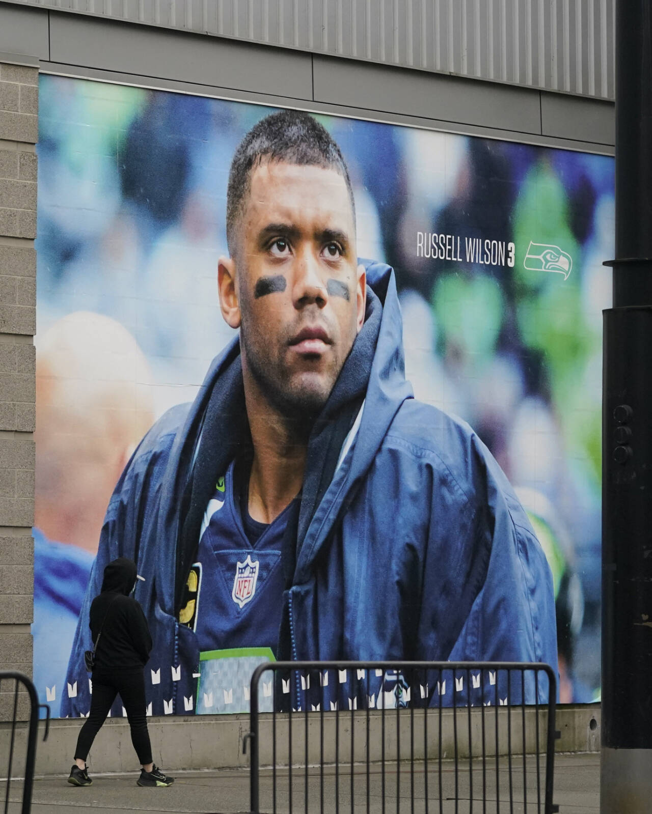 A pedestrian walks past a photo of Seattle Seahawks quarterback Russell Wilson at Lumen Field, Tuesday, March 8, 2022, in Seattle. The Denver Broncos agreed to send a massive haul of players and draft picks to the Seattle Seahawks in a trade for Wilson, two people familiar with the negotiations confirmed to The Associated Press on Tuesday. The blockbuster trade, which is pending Wilson passing a physical, can’t become official until the start of the new league year on March 16, 2022. (Ted S. Warren/The Associated Press)