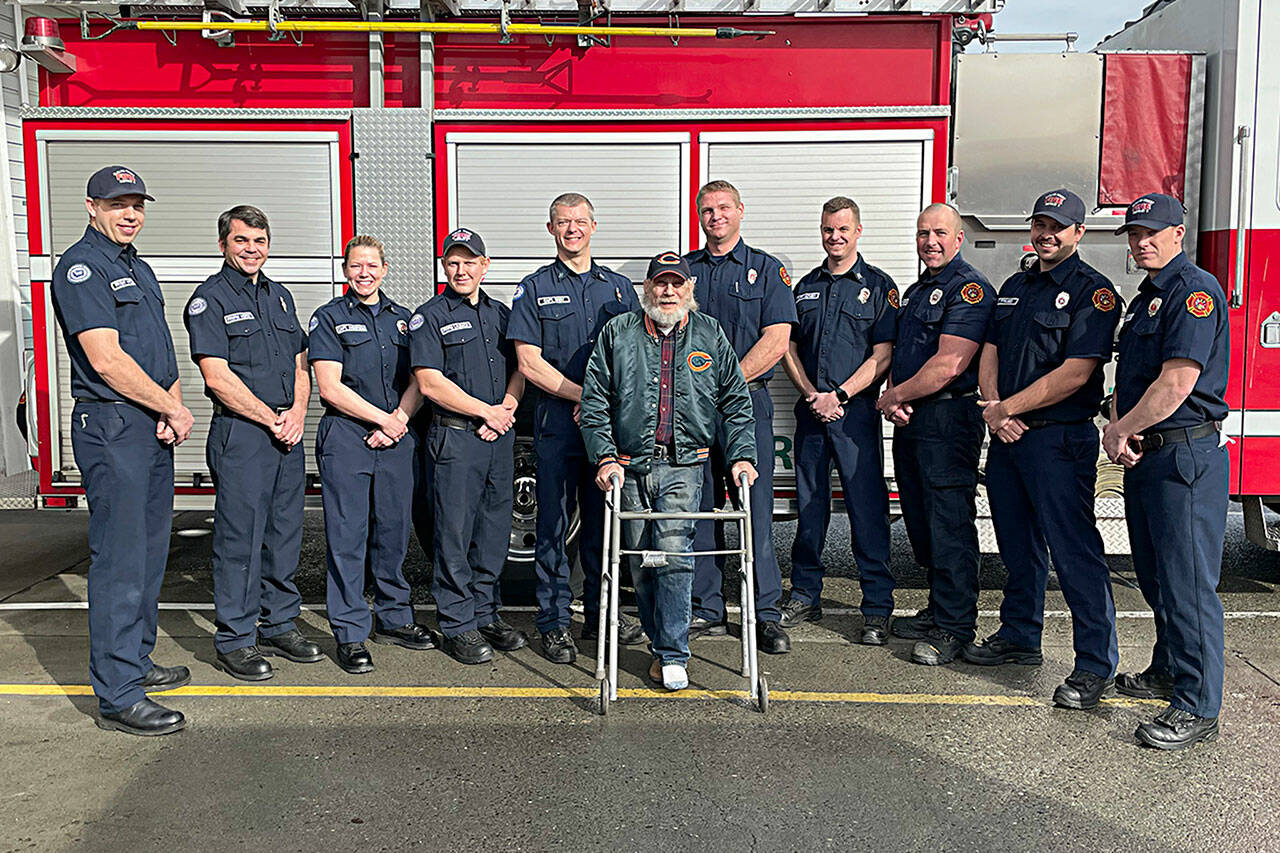 Clallam County Fire District 3 firefighters meet with Gregg Vella weeks after rescuing him from a house fire. Pictured from, left, are firefighter/EMT Jaisal White; firefighter/paramedic Len Horst; Capt. Stef Anderson; firefighter/paramedic Chase Laubach; Capt. Kjel Skov; Vella; firefighter/paramedic Mark Mullvain; Capt. Joel McKeen; firefighter/EMT Jared Romberg; firefighter/paramedic Casey Sires; firefighter/paramedic Jack Hueter. (Matthew Nash/Olympic Peninsula News Group)