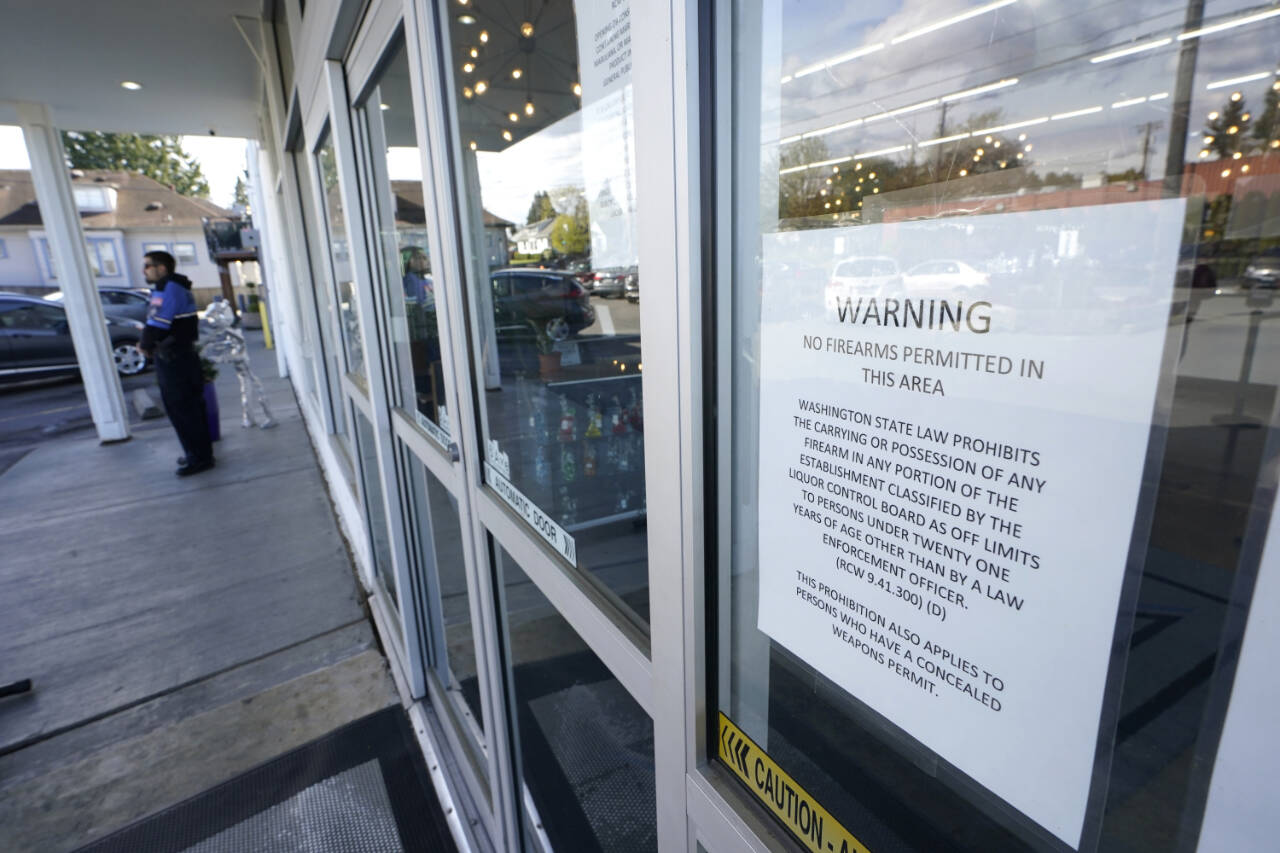 A sign warns that firearms are prohibited at Mary Mart, a marijuana store, Tuesday in Tacoma as armed security guard Austin MacMath stands watch outside at left. A surge in robberies at licensed cannabis shops in Washington state is helping fuel a renewed push for federal banking reforms that would make the cash-dependent stores a less appealing target. (AP Photo/Ted S. Warren)