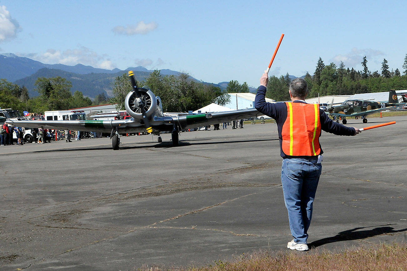 Tom Wayne Duke of Langley directs traffic as a North American SNJ-5 Texan based in Diamond Point taxies into a parking spot on Saturday at William R. Fairchild International Airport as part of Armed Forces & Public Safety Airport Appreciation Day and Fly-in. The event featured a variety of modern and vintage aircraft, flying demonstrations, public saftey displays and Young Eagles flights for children. (Keith Thorpe/Peninsula Daily News)