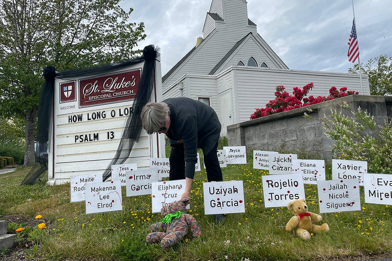 The Rev. ClayOla Gitane, rector at St. Luke’s Episcopal Church, places signs and teddy bears in memory of the 21 victims of Tuesday’s mass shooting at Robb Elementary School in Uvalde, Texas. (Matthew Nash/Olympic Peninsula News Group)