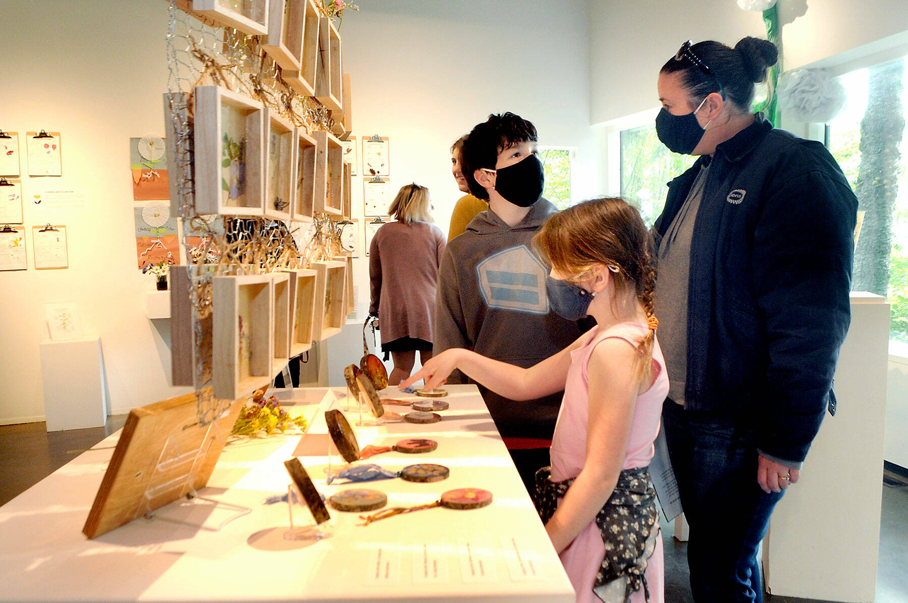 Alice Cordery, 7, a first-grade student at Jefferson Elementary School in Port Angeles, front, points to an artwork as her brother, Pat Cordery, 11, and mother, Teresa Cordery, follow along during an opening gala for Blooming Artists, an exhibition of nature-related art pieces on Tuesday at the Port Angeles Fine Arts Center. (Keith Thorpe/Peninsula Daily News)
