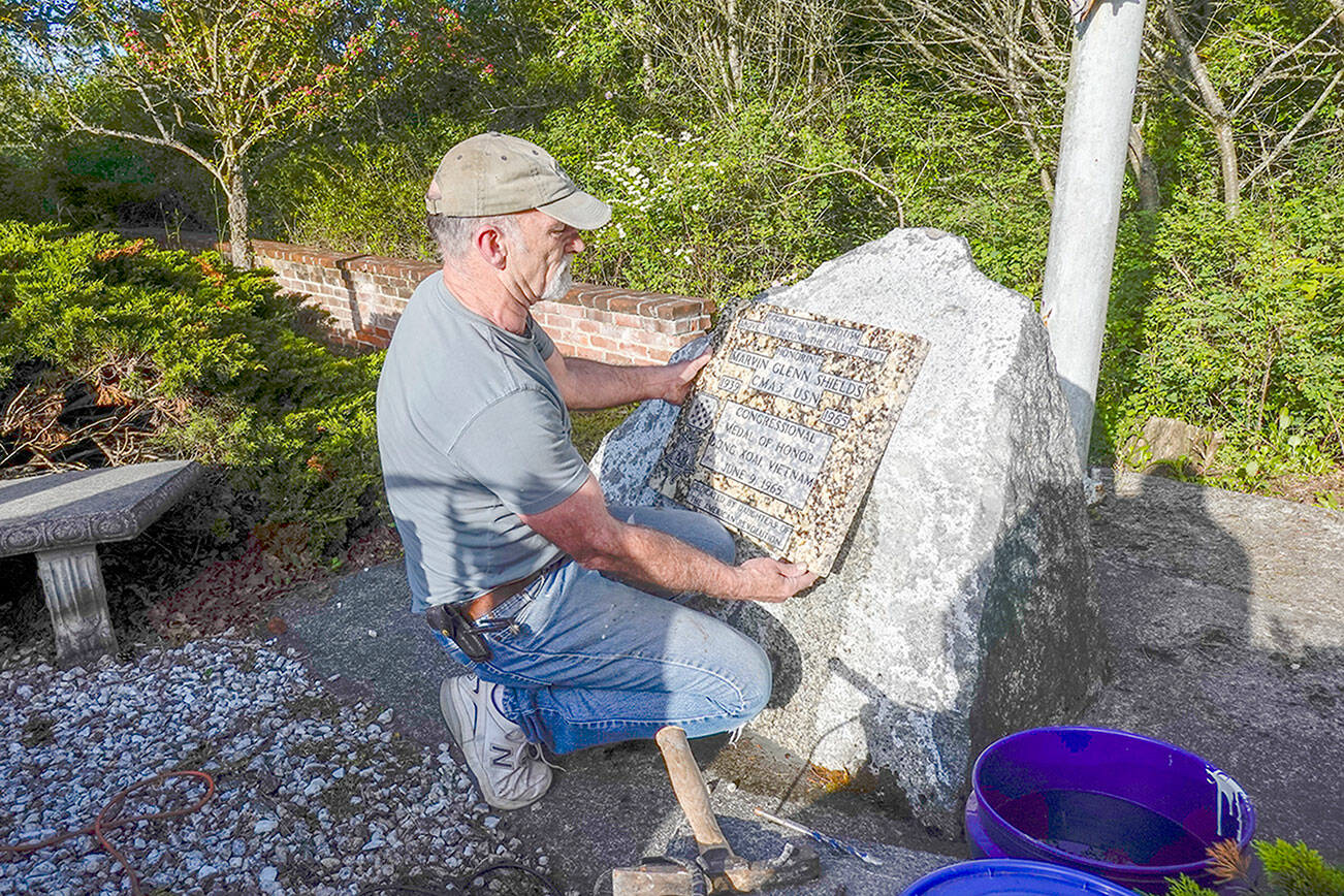Robert Parker, a self-employed contractor from Port Orchard, installs a granite plaque honoring Navy Seabee Marvin G. Shields, who died in June 1965 in Vietnam and was awarded the Medal of Honor for heroism, at the Marvin Shields Memorial Flagpole on a stone monument from which the original bronze plaque was stolen in 2019. “He is very precious to us,” said Parker, an ex-Navy Seabee who volunteered to place the plaque. “This plaque is granite so there is less incentive for thieves,” he added. The Admiralty Inlet Chapter of the Daughters of the American Revolution will dedicate the memorial plaque at 1 p.m. Saturday in the small park on the north side of West Sims Way between Sheridan and Tenth streets. (Steve Mullensky/for Peninsula Daily News)