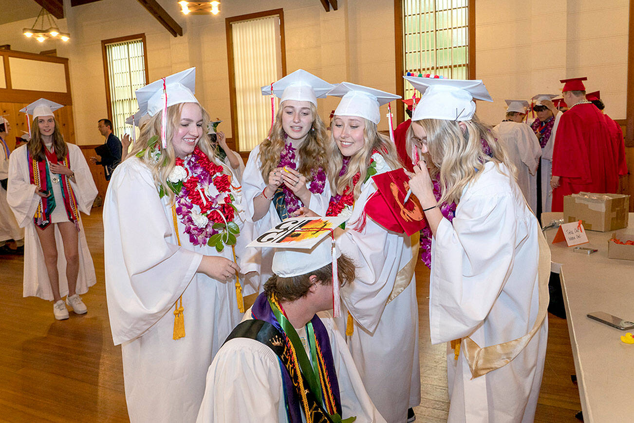 Port Townsend High School’s Sidda Hayes, Macy Smith, Charlotte Falge and Maddi Witheridge look over Tusker Behrenfeld’s mortar board to decipher the meaning. Eighty-two seniors received their diplomas before family and friends during the 132nd Commencement at McCurdy Pavilion on Friday night. (Steve Mullensky/for Peninsula Daily News)
