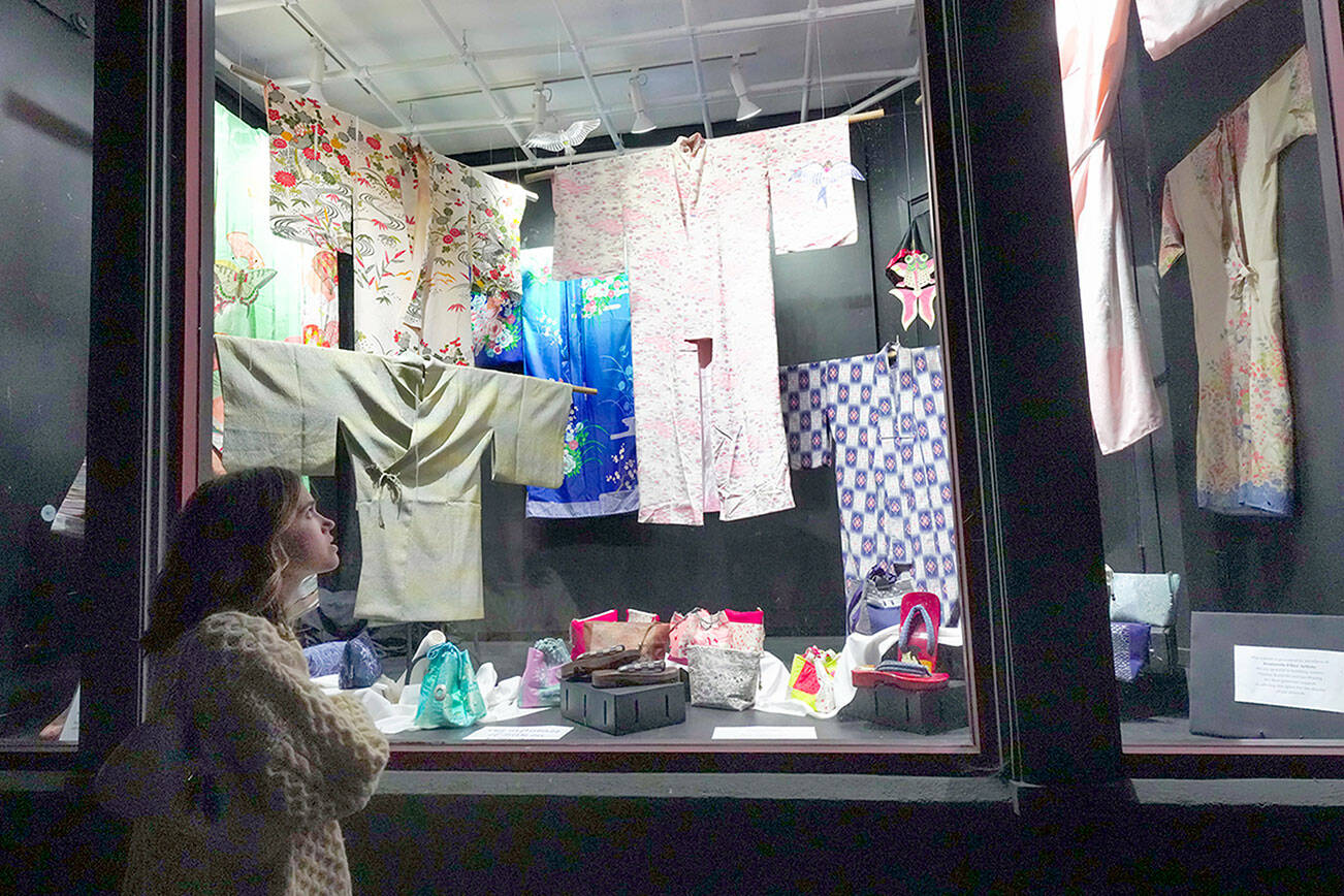 Abbey Engrav, visiting Port Townsend from New York City for her brother’s wedding on Saturday, looks at the vintage Japanese garments and shoes on display at the Peninsula Fiber Artists display window on Tyler Street in the Uptown Neighborhood on Friday night. (Steve Mullensky/for Peninsula Daily News)