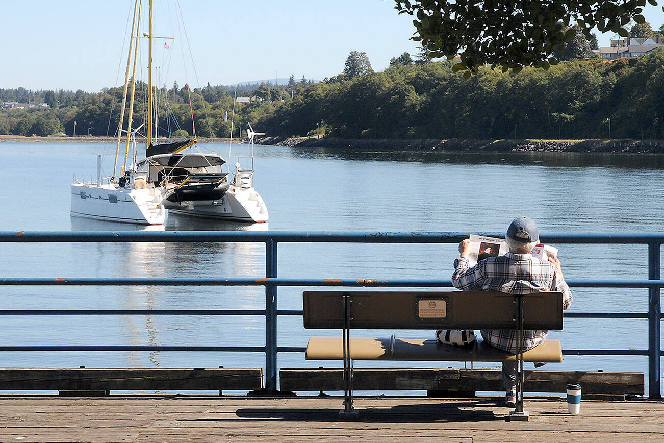 KEITH THORPE/PENINSULA DAILY NEWS
Ingrid Sorensen of Port Angeles reads a magazine on a park bench at Port Angeles City Pier on Tuesday as a catamaran sits at anchor just offshore in Port Angeles Harbor. As summer begins to give way to autumn, the forecast calls for seasonal conditions across most of the North Olympic Peninsula.