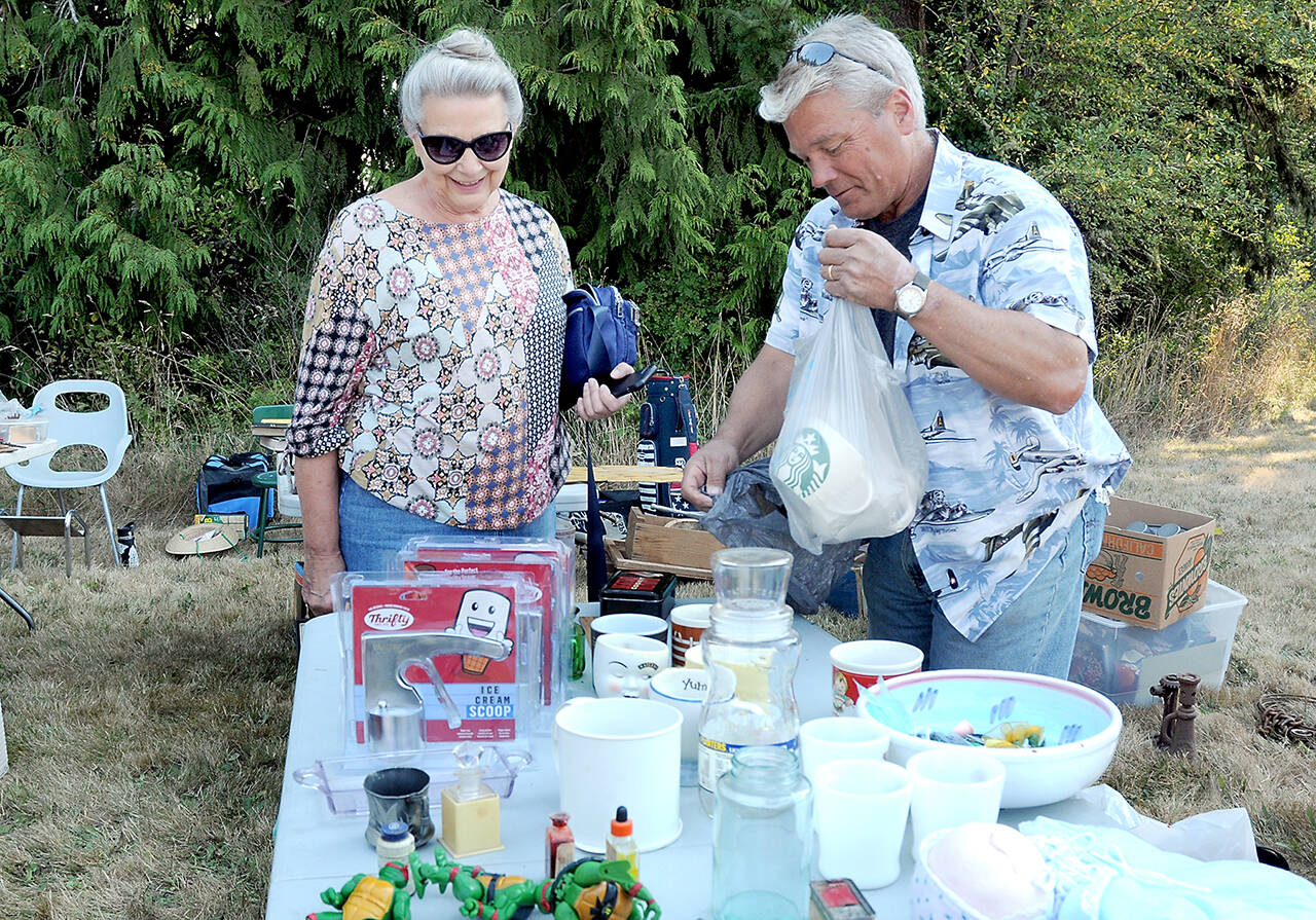 Marlene McCurdy of Port Angeles, left, purchases coffee mugs from Gary Gort of Port Angeles at a sale table in front of the Crescent Grange Hall in Joyce on Saturday. (Keith Thorpe/Peninsula Daily News)