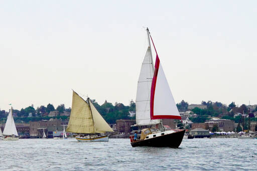 Sailboats cruise by the downtown area of Port Townsend to end the 45th Wooden Boat Festival at Point Hudson Marina on Sunday. (Steve Mullensky/for Peninsula Daily News)
