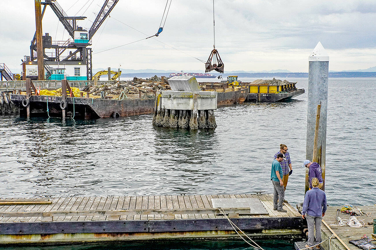 A crew from the Northwest Maritime Center facilities department, Sam Trocano, Jeff Hogue, Shane Meyer and Mike Conklin, work on the removal of the floating dock on the center’s pier in preparation of winter winds and weather. In the background, work continues on the deconstruction of the entrance to the Point Hudson Marina by Orion of Tacoma. (Steve Mullensky/for Peninsula Daily News)