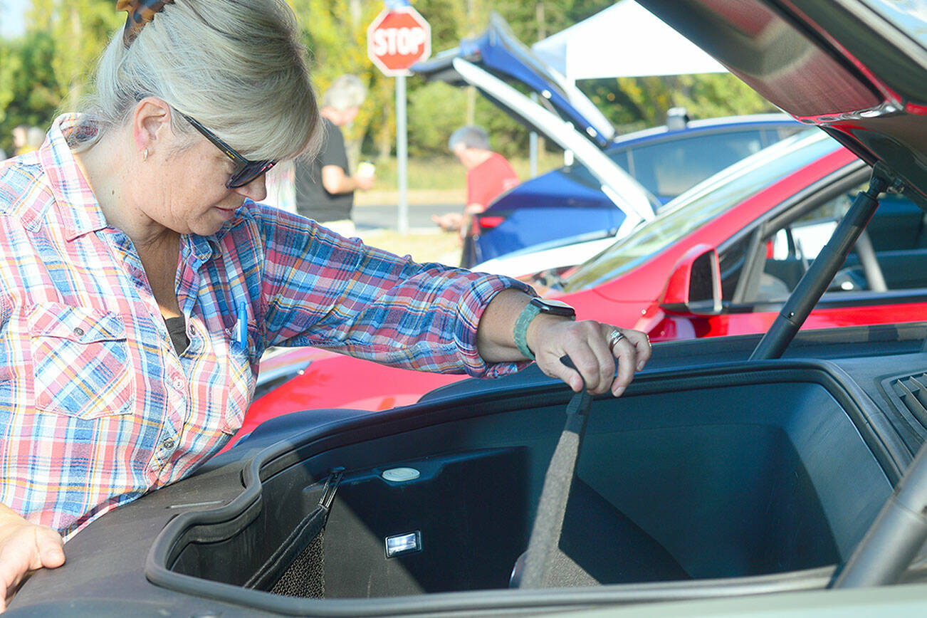 Wendy Davis of Port Townsend takes a look under the hood of her Rivian truck, where an empty storage area is where the engine would have been on a gasoline-powered car. The Rivian’s battery is on the bottom of the truck, much like a skateboard, Davis said. The vehicle can travel 320 miles on a charge, she added. (Diane Urbani de la Paz/For Peninsula Daily News)