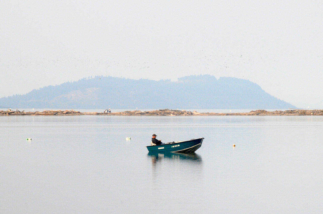 A boat floats placidly on Dungeness Bay on Saturday as hikers walk along Dungeness Spit in the background and Striped Peak stands on the horizon. Unseasonably warm and dry conditions made for good boating weather, despite hazy skies from wildfire smoke from east of the Cascades. (Keith Thorpe/Peninsula Daily News)