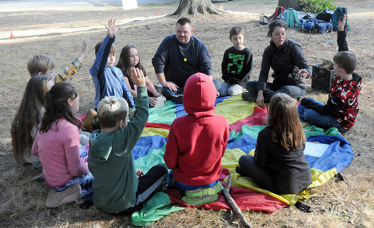 Seaview Academy instructor Eric Pickens, top, and Olympic Nature Experience teacher Amanda Erickson, right, sit with Outdoor, Real-world, Child-centered Academic Program students during an outdoor gathering at Lincoln Park in Port Angeles. (Keith Thope/Peninsula Daily News)