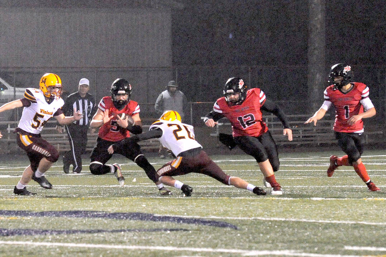 Lonnie Archibald/for Peninsula Daily News
Neah Bay's Jullian Carrick (5) looks for running room against Winlock Friday night on the Spartan Stadium turf in Forks during this Class 1B playoff game.  Also in the action are Red Devils Charles Halttunen (12) and Jodell Wimberly (1).  Winlock's Dalton Noyes ( 54) and Logan Hall (20) were on the defense.