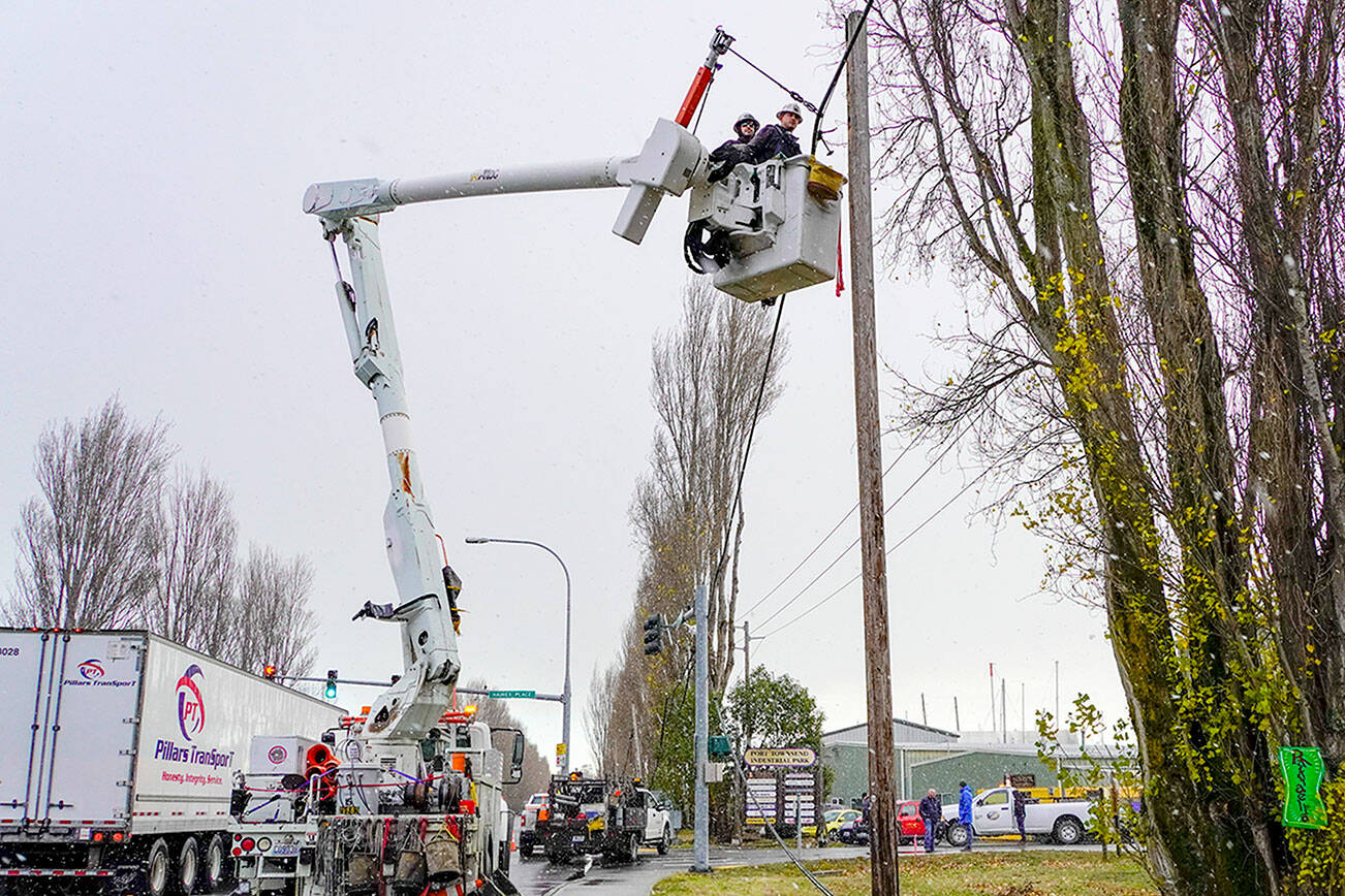 Joe Suter and Dave Smith, employees of Palouse Power, which contracts for additional services to Jefferson County Public Utility District, have snow flurries fall on them as they work to lift a communications cable, owned by Lumen, that was torn down Sunday morning by a boat on a trailer that snagged the cable at the entrance as it entered the boat yard, workers said. The PUD secured the cable as a public service so the entrance could be opened for business on Monday. (Steve Mullensky/for Peninsula Daily News)