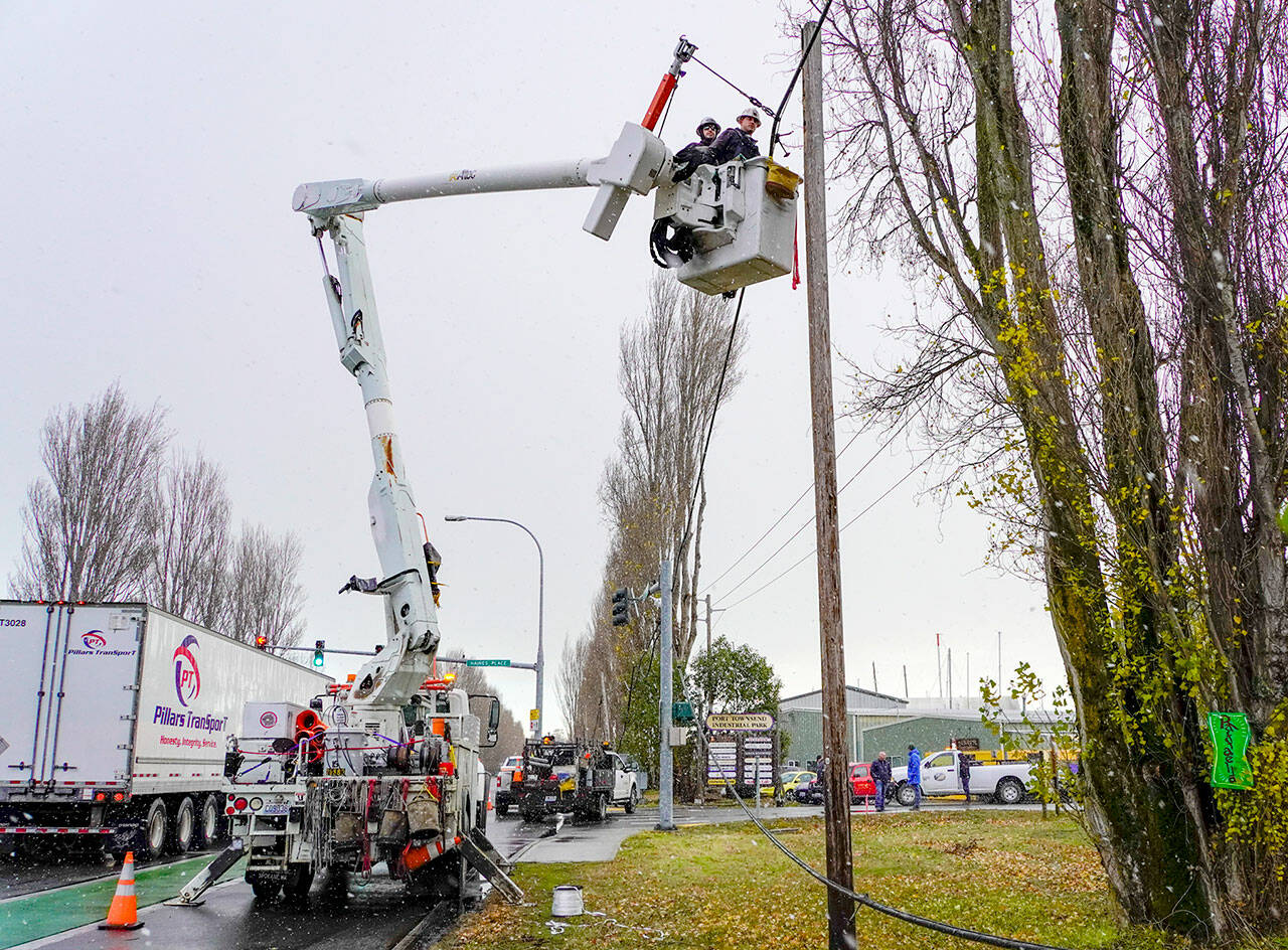 Joe Suter and Dave Smith, employees of Palouse Power, which contracts for additional services to Jefferson County Public Utility District, have snow flurries fall on them as they work to lift a communications cable, owned by Lumen, that was torn down Sunday morning by a boat on a trailer that snagged the cable at the entrance as it entered the boat yard, workers said. The PUD secured the cable as a public service so the entrance could be opened for business on Monday. (Steve Mullensky/for Peninsula Daily News)