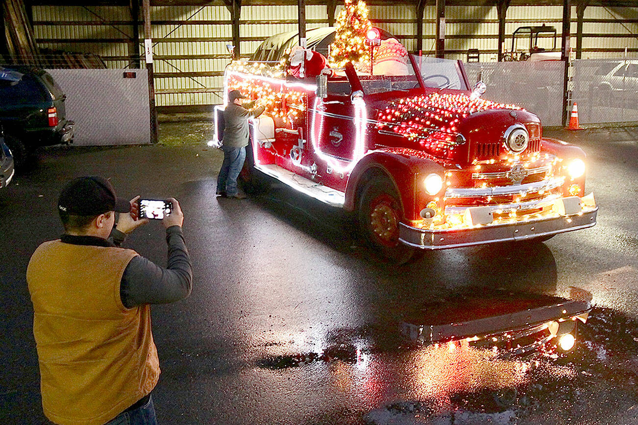 Tyler Gage photographs a fire engine while Adam DeFilippo finishes decorating the old fire engine in preparation for two Operation Candy Cane programs in Port Angeles. (Dave Logan/for Peninsula Daily News)