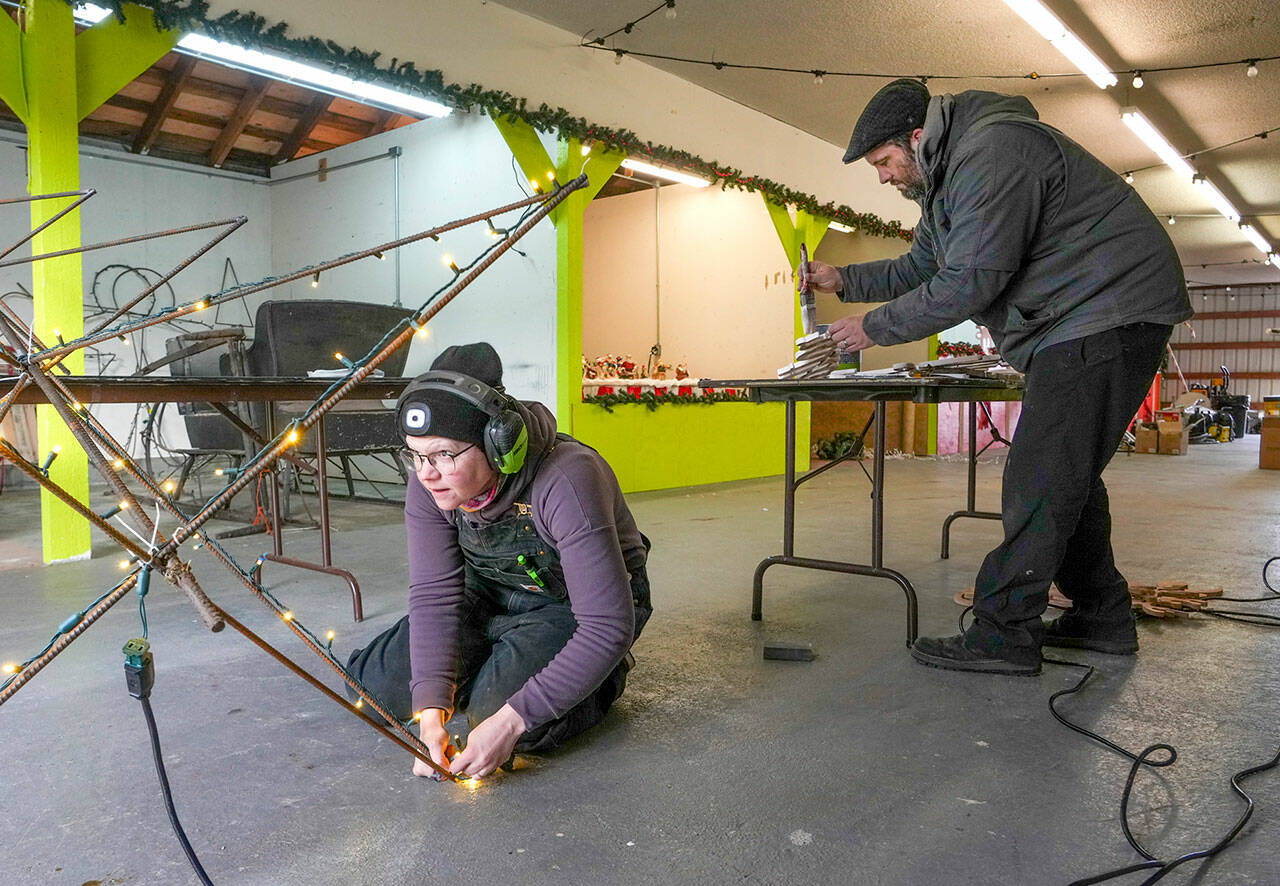 Lilly Gulden checks that the are lights are glowing on a metal Christmas tree skeleton while Jefferson County Fairgrounds manager Danny McEnerney paints lettering for a display all in preparation of the opening of the Magic of Christmas event at the fairgrounds on Thursday. (Steve Mullensky/for Peninsula Daily News)