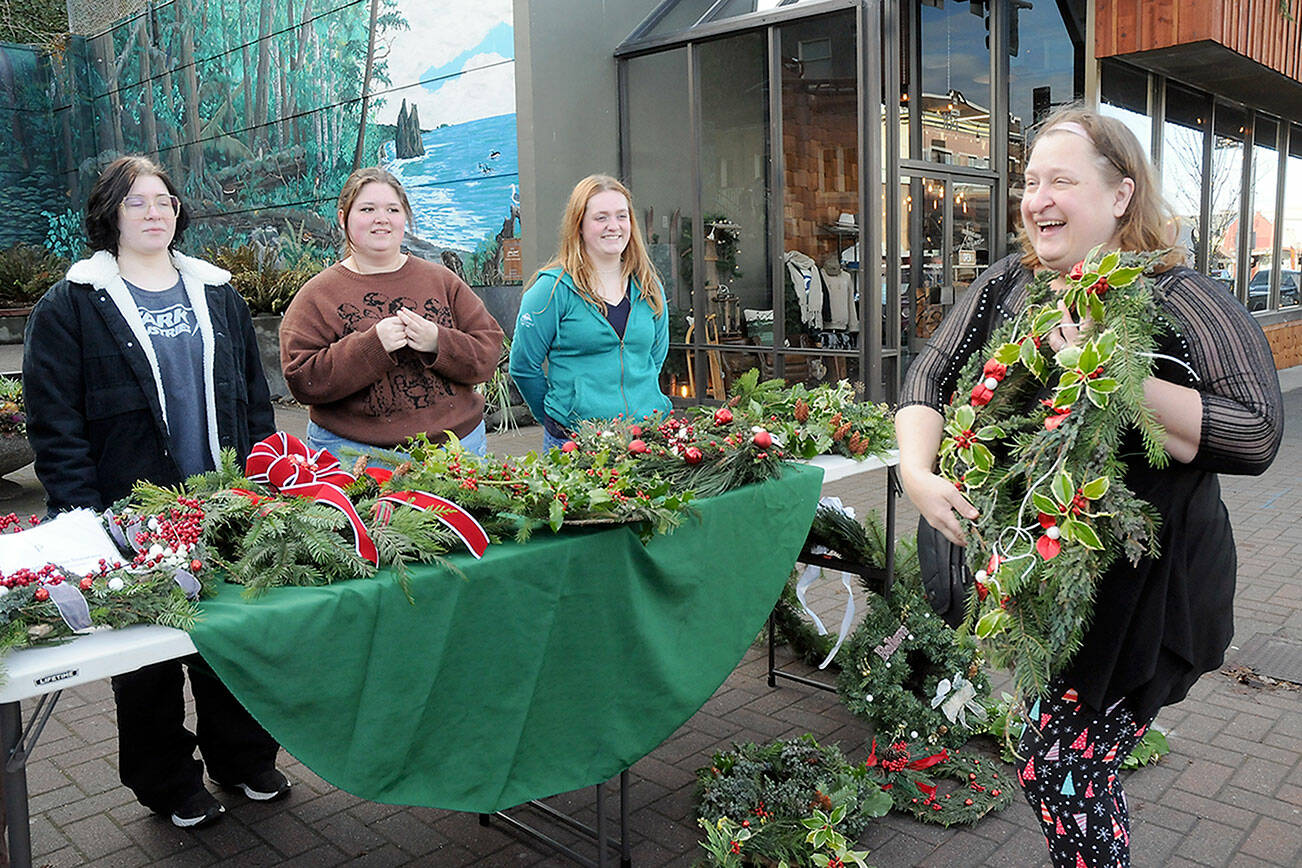Louisa Monger of Port Angeles, right, shows off a handmade wreath she was purchasing at tables staffed by members of the Port Angeles High School Choir, including seniors, from left, Kaelyn Herringer, Rayna Mathison and Grace Possinger, on Saturday at the Conrad Dyar Memorial Fountain in downtown Port Angeles. The wreath sale was a benefit to help fund a spring trip to perform at Carnegie Hall in New York with members of the school’s choir, orchestra and band. Leftovers from Saturday’s sale, along with a bake sale and silent auction, will be available during the school’s holiday concert at 7 p.m. tonight at the Port Angeles Performing Arts Center, 304 E. Park Ave. (Keith Thorpe/Peninsula Daily News)