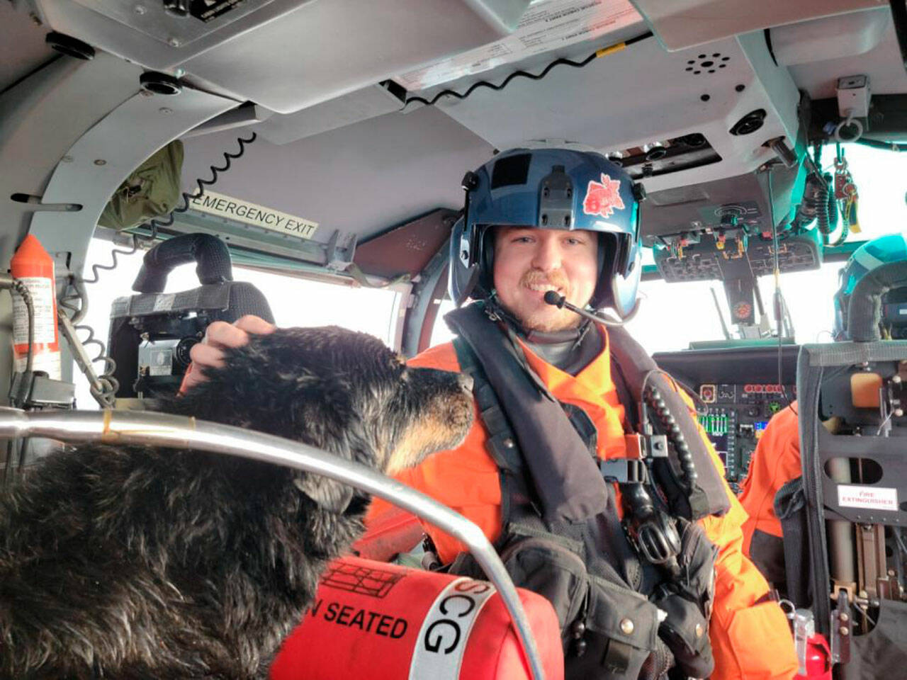 Petty Officer 3rd Class Austen Marshall, an avionics electrical technician and a flight mechanic at Coast Guard Air Station Port Angeles, sits near a dog his aircrew rescued from a grounded sailing vessel near Vancouver Island, British Columbia. The aircrew rescued one person and two dogs from the vessel. (U.S. Coast Guard courtesy photo)