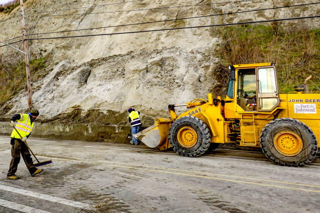 Port Townsend employees Chris MacDonald, left, and Rafe Thornton, clean up the last of the tons of dirt from a landslide that occurred on Water Street in Port Townsend about 4 a.m. Monday. The road was closed and vehicular traffic was diverted to other streets. It took 18 trips of 5-yard capacity dump trucks to remove the dirt and haul it to a facility on Redwood Street. (Steve Mullensky/for Peninsula Daily News)