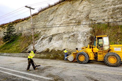 Port Townsend employees Chris MacDonald, left, and Rafe Thornton, clean up the last of the tons of dirt from a landslide that occurred on Water Street in Port Townsend about 4 a.m. Monday. The road was closed and vehicular traffic was diverted to other streets. It took 18 trips of 5-yard capacity dump trucks to remove the dirt and haul it to a facility on Redwood Street. (Steve Mullensky/for Peninsula Daily News)