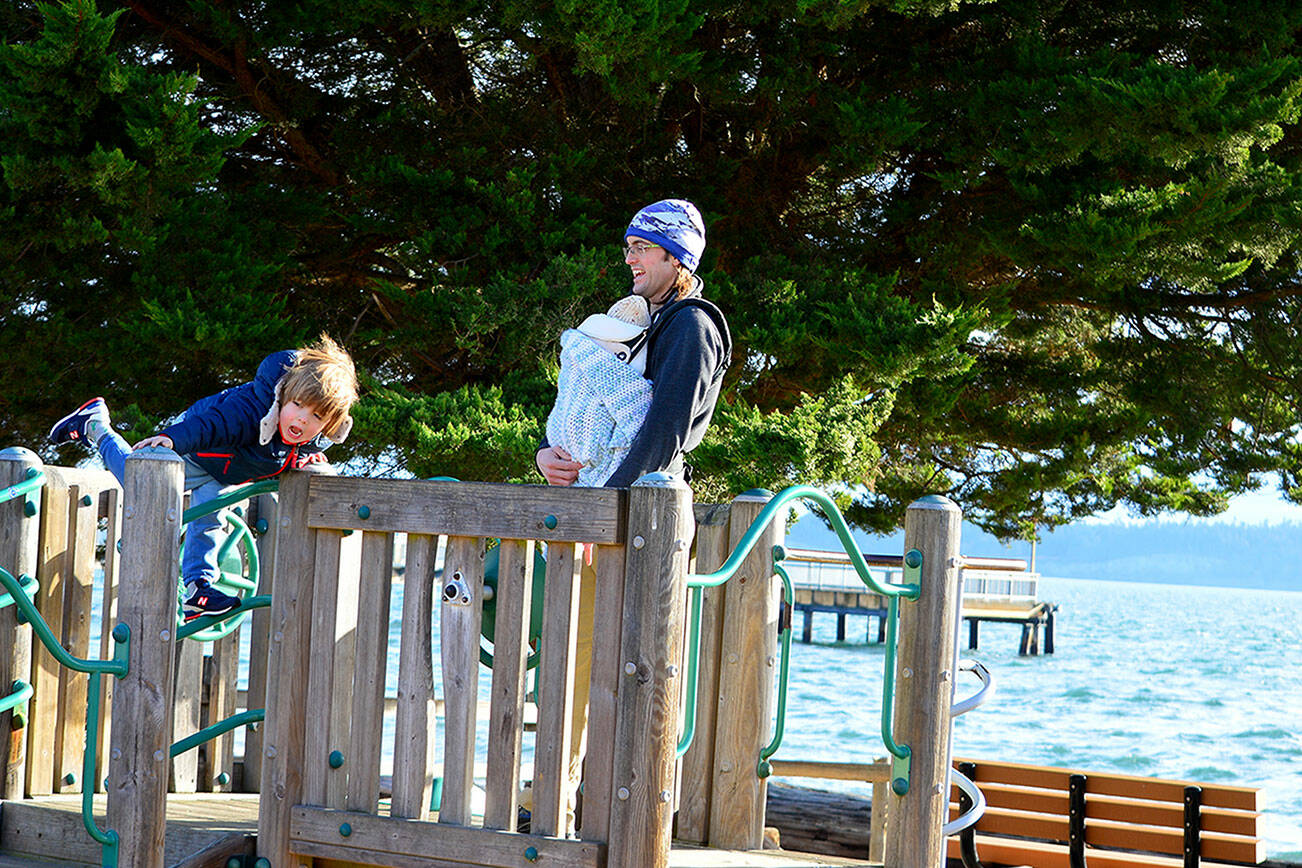 Roarke Jennings of Port Townsend, along with son Niko and baby Chiyo, take in the sun and wind at Pope Marine Park in downtown Port Townsend on Wednesday morning. (Diane Urbani de la Paz/For Peninsula Daily News)