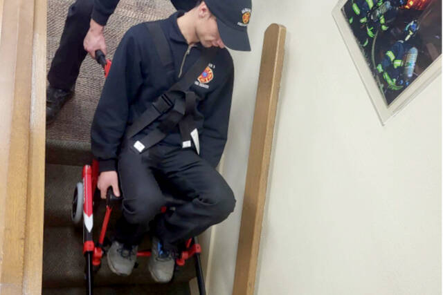 Captain/EMT Tyler Gear, at top, and Firefighter/Paramedic Margie Brueckner, bottom, train on Clallam 2’s new stair chair by lowering Recruit Theo Saxe down a flight of stairs.