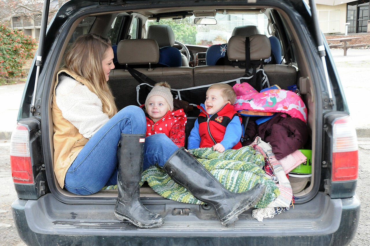 Katie Roszatycki of Port Angeles and her children, June Roszatycki, 2, and Asher Roszatycki, 3, sit in the back of their car waiting for the delivery of dry shoes and socks from another family member after an outing to Hollywood Beach on Thursday. The family was keeping themselves entertained in the parking lot at Port Angeles City Pier. (Keith Thorpe/Peninsula Daily News)