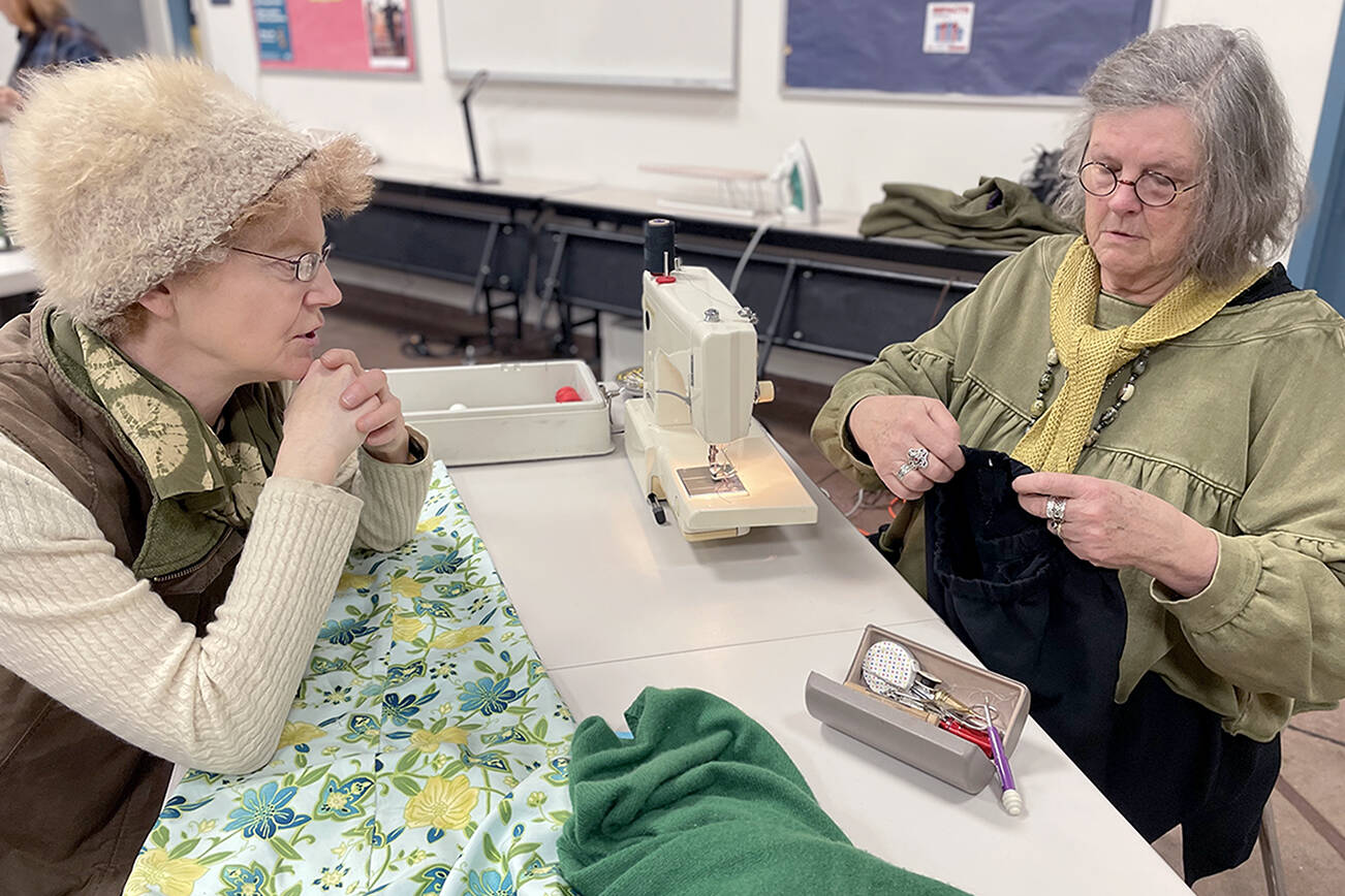 Loran Scruggs, left, brought a green cashmere sweater, a pair of floral silk pants and a pair of black cotton pants that needed to be mended to the Port Townsend Marine Science Center’s Repair Cafe. Paula Lalish was one of three volunteers on hand to assist people by fixing clothing that had holes, rips, tears and and broken zippers. (Paula Hunt/Peninsula Daily News)