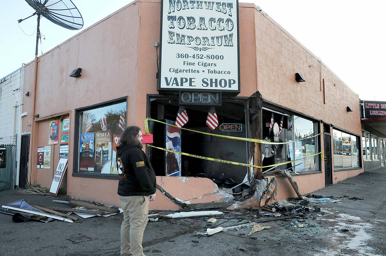 Justin Brophy, general manager of Northwest Tobacco Emporium, at 309 E. First St. in Port Angeles, examines the front of the establishment on Wednesday morning after a car crashed into the building and caught fire late Tuesday night. (Keith Thorpe/Peninsula Daily News)