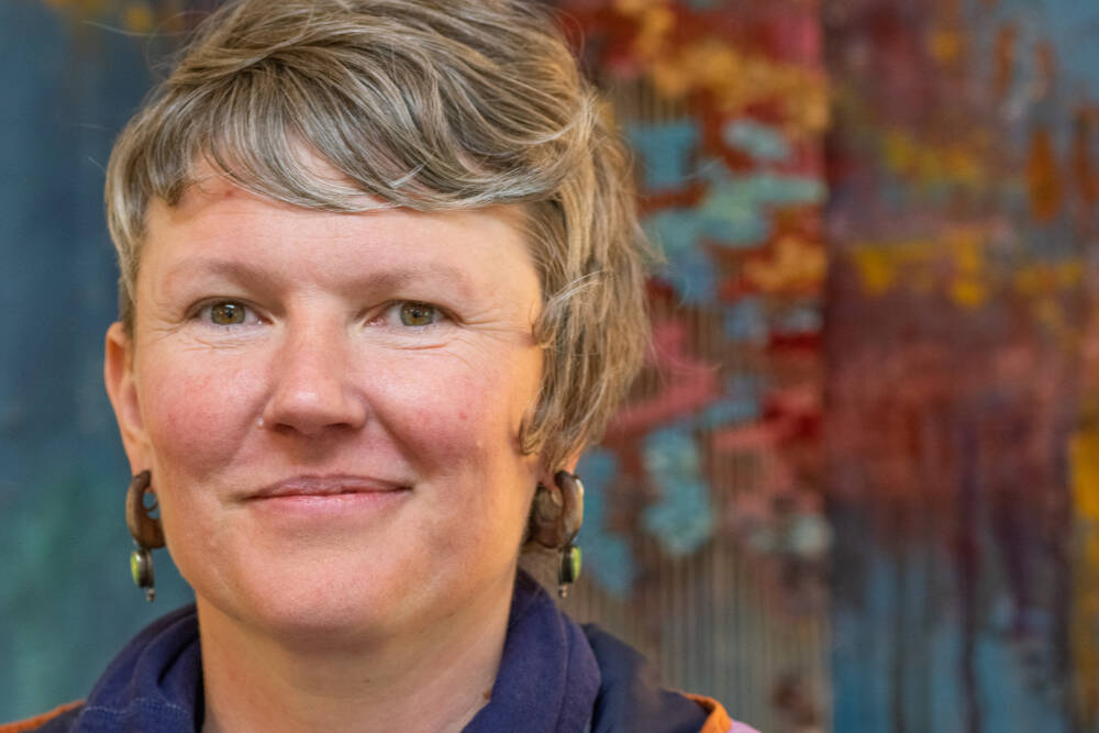 Artist Emily Carlquist, seen here before one of her abstract multi-media pieces featuring acrylic paint on textured canvas with needle-woven local fiber warped on canvas, on display at Dandelion Botanical for the month of April. (Emily Matthiessen/Olympic Peninsula News Group)