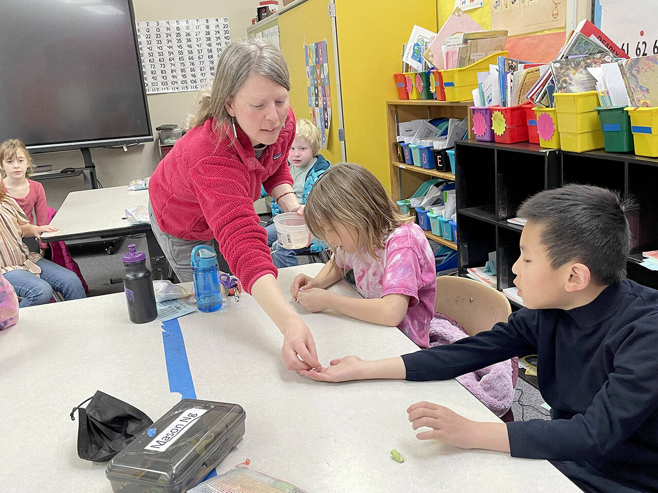 Mandy Miller hands first-grader Mason Ng a bean in teacher Jennifer Soule’s class at Franklin Elementary School. Cora Lehmann, right, peels a bean apart to find and identify the different parts of the seed as part of a lesson in the Creative Start program administered by the Port Angeles Fine Arts Center in three district schools that combine lessons in art and science. (Paula Hunt/Peninsula Daily News)